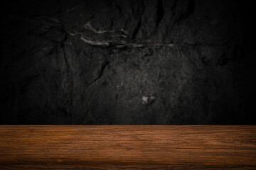 Free space on a wooden table for displaying products with a blurred black wall background.