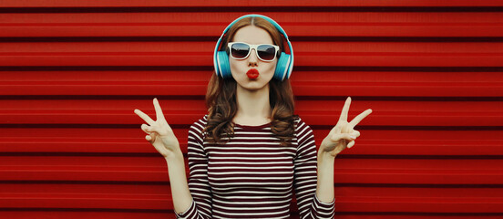 Portrait of young woman in wireless headphones listening to music on a red background