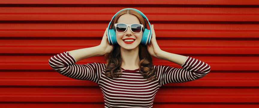Portrait of happy young woman with wireless headphones listening to music on a red background