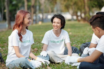 Young volunteers resting on grass in park after picking up trash in local park