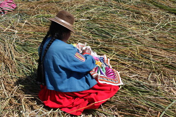 Indigenous lady from titicaca lake in south america is stitching a colorful handcraft on the floating island