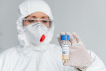 Coronavirus vaccine in hand of scientist in protective uniform blurred on background