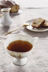 White Porcelain Cup of tea and Slices of Pound Loaf Cake with raisins on plate on greige linen tablecloth. Selective focus