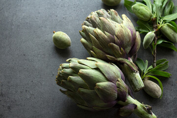 Uncooked artichokes on a table. Gray textured background with copy space. Organic vegetables top view photo. Healthy eating concept. 