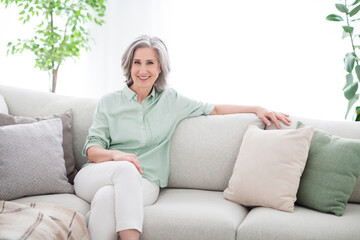 Photo of charming attractive positive old woman smile good mood sit couch indoors inside house apartment