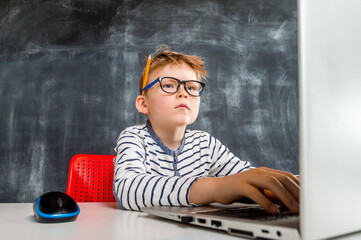 Smart nerd kid boy with laptop computer. Student in glasses is programming while sitting at desk....