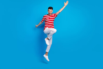 Fototapeta na wymiar Full length photo of cheerful young man raise hands jump up air isolated on pastel blue color background