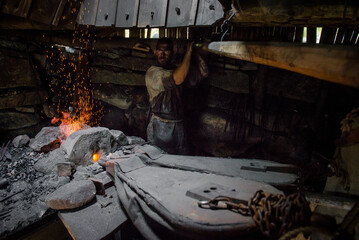 blacksmith at the stove. A man with a dirty face burns iron at the furnace 