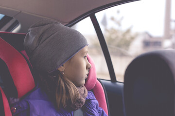 Little girl sit in the car seat and looks out the window