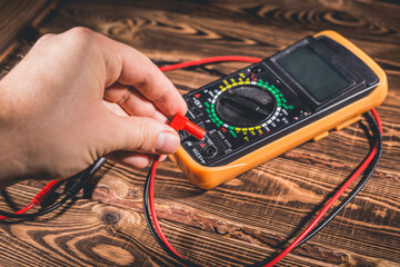 Multimeter and two test leads on a wooden background. A man's hand holds two test leads. A studio...
