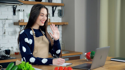 Smiling woman chef teacher in beige apron greets housewife student teaches online remote video call...