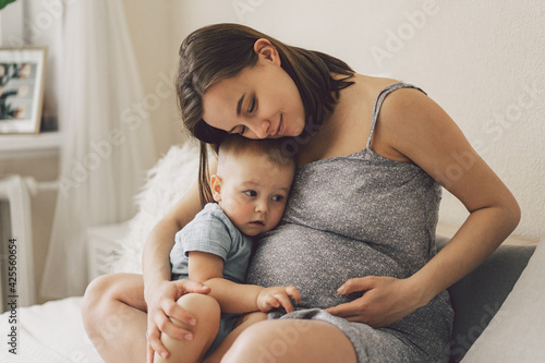 Young woman with her first child during second pregnancy. Motherhood and parenting concept. Toddler boy and mom.