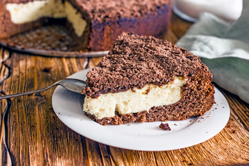 A piece of homemade chocolate pie with curd filling on a plate on a wooden table, close-up
