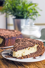 A piece of homemade chocolate pie with curd filling on a plate on a wooden table, close-up