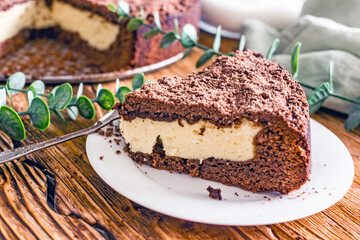 A piece of homemade chocolate pie with curd filling on a plate on a wooden table, close-up