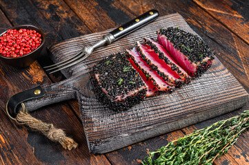 Homemade Cut Grilled Sesame Tuna steak on a cutting board. Dark Wooden background. Top view