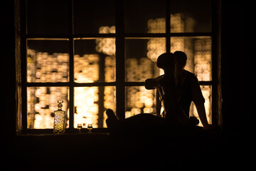 A realistic dollhouse living room with furniture and window at night. Romantic couple sitting on window. Artwork table decoration with handmade realistic dollhouse. Selective focus.