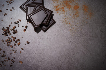 Pieces of dark chocolate with raw cacao nibs and cocoa powder on grey stone background. High quality chocolate bar treat. Side borders from top view. Empty space for text. Copy space.