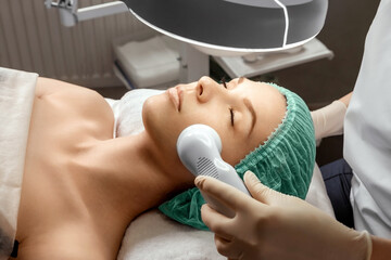 The beautician cleans the girl's skin with a special apparatus with light. The concept of facial...