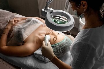 The beautician cleans the girl's skin with a special apparatus with light. The concept of facial...
