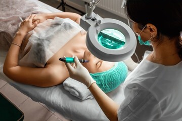 A beautician wearing medical gloves cleans the pores on the face using special equipment while...