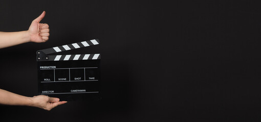 Hand is holding black clapperboard or movie slate and do like hand sign.It is used in film production and cinema,movies industry on black background. - obrazy, fototapety, plakaty
