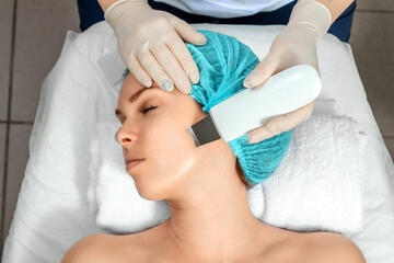 A gloved beautician cleanses the skin on the face using a special gel and equipment. The concept of...