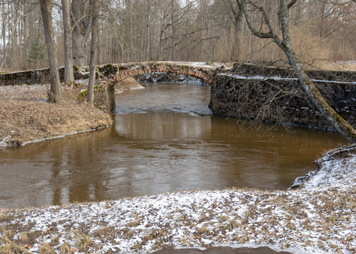 a continuous boulder stone bridge with a brick used for masonry, early spring, bare trees, snow plan on the ground, Stone arch bridge over the river Kuja, Madona, Latvia