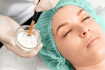 A beautician applies a mask to the face in a beauty salon. The concept of facial hygiene, cosmetic...