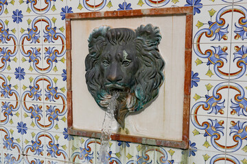 A water feature with a lion's head on a ceramic tile background in a public plaza in Estepona in Spain