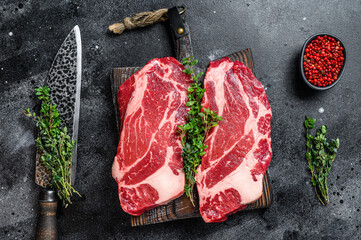 Raw chuck eye roll steaks premium beef meat on a cutting board. Black background. Top view