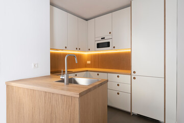 Encimera de madera con fregadero y mueble de cocina blanco al fondo iluminado con luz led.