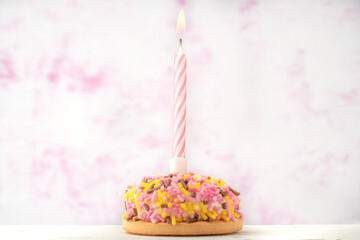 small birthday cake with one candle over soft pink background with copy space