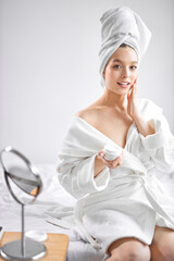 pretty and beautiful. relaxed woman after shower doing beauty procedures, applying cream on face and neck