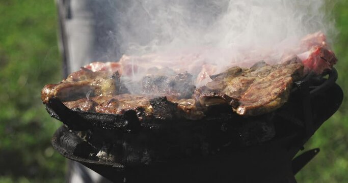 Close up shot of a sizzling hot barbecue with a man flipping the meat on a beautiful warm sunny spring day