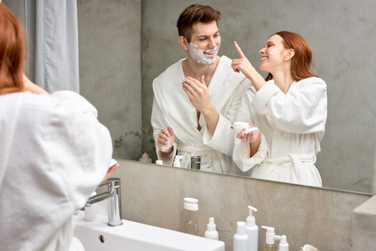 Interracial Couple Take Care Of Facial Skin, Woman Applying Cream While Man Is Going To Shave Stubble