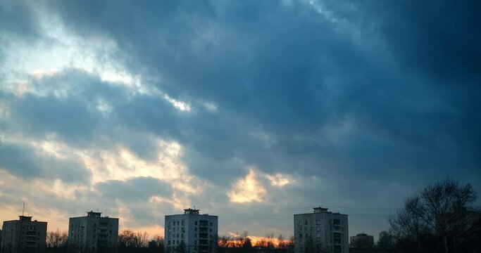 Time lapse of evening dark clouds over the residential buildings of the town at sunset.