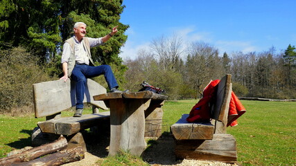 aktiver Senior macht Rast bei einer Wanderung auf einer Bank in der Natur an einem sonnigen Tag
