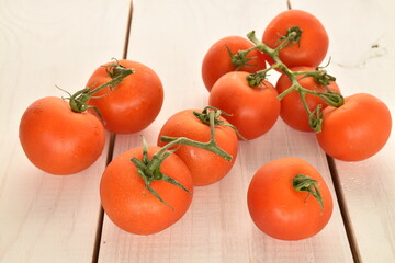 Several ripe, bright red, organic, delicious cocktail tomatoes, close-up, on a table made of natural wood.