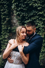 Walk of the bride and groom in the summer park. Newlyweds in seclusion. He and she against the backdrop of green foliage.