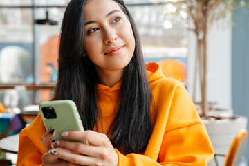 Smiling asian woman using mobile phone while sitting in cafe