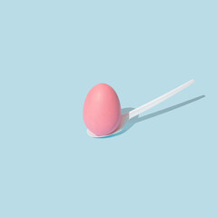 Fototapeta na wymiar Pastel pink Easter egg on white plastic spoon. Trendy, creative and minimal spring concept.