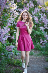Obraz na płótnie Canvas beautiful girl in a short purple dress walks in the lilac garden, leather dress, lilac bloom