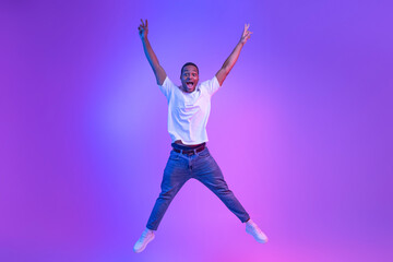 Fototapeta na wymiar Unlimited Fun. Emotional Funny Black Guy Jumping With Hands Up, Neon Light
