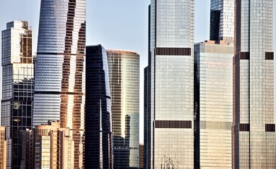 The bright sunset sky and sun glare are reflected in the glass facades of tall skyscrapers....