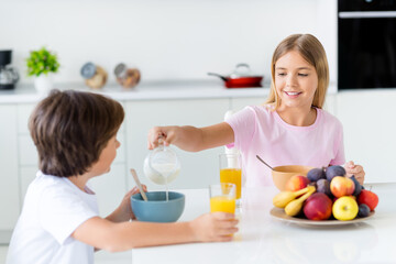 Photo of happy smiling charming pretty sister taking care of little brother eating breakfast drinking juice at home house