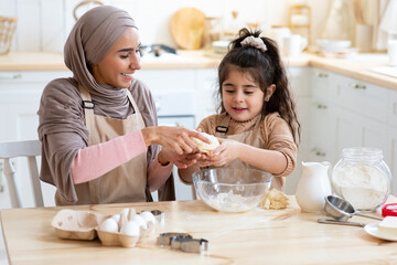 Obraz na płótnie Canvas Happy arab mom and her little daughter kneading dough together in kitchen