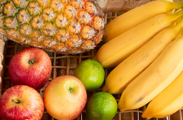 Pineapple, bananas, apples, limes in a basket