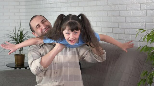 Make a plane with father. A happy dady play with her child and little girl makes a plane with father in the room.