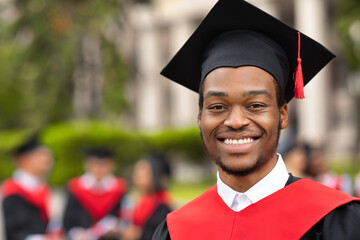 Cheerful african american guy in graduation costume, closeup portrait